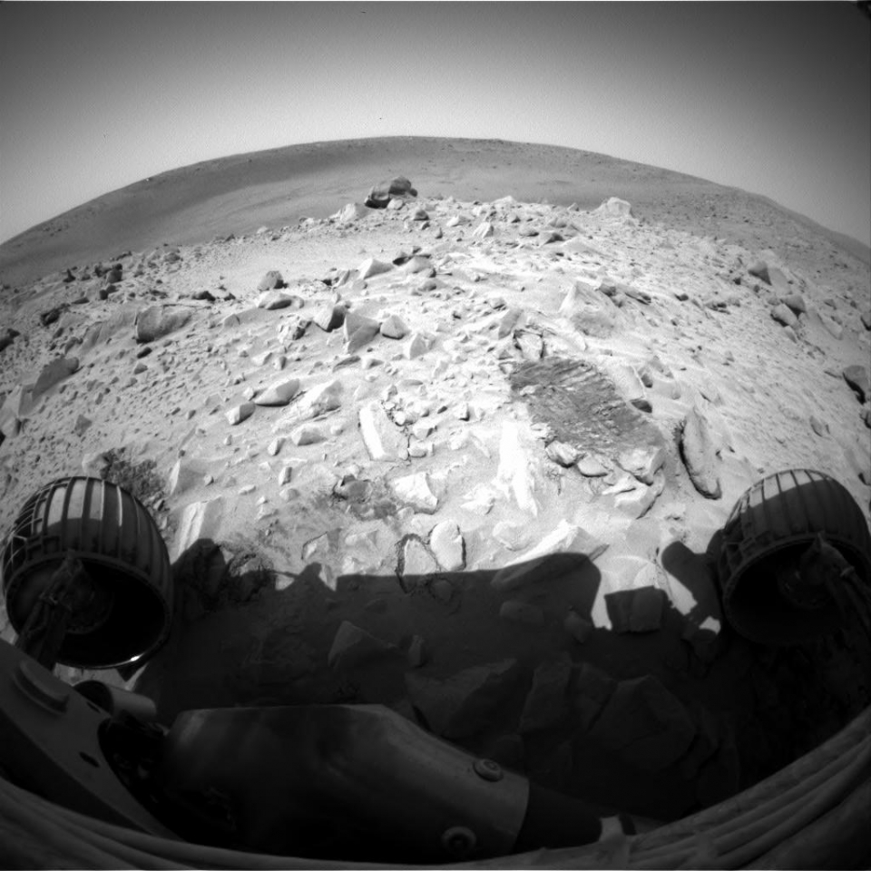 Figure 1. Spirit at the crater rim. Notice the large light colored rock on the crater rim to the right. Enhanced version of a full frame EDR (Experiment Data Record) image taken by Spirit on Sol 67 using the front left hazard avoidance camera mounted on the main rover body .52 meters (20.47 inches) above the Martian surface. The HazCam fisheye lenses have a focal length of 5.58 mm at the center of the field and operate at f/15 with a diagonal field of view of 180º. Compare the appearance of the rock in this image versus sol 66.